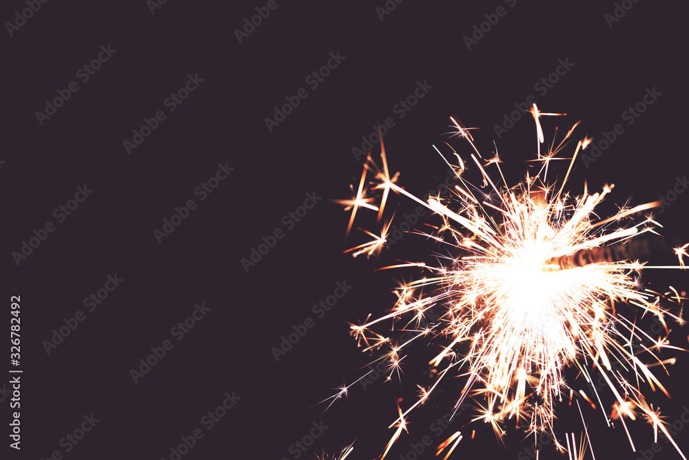 closeup view on burning sparkler in front of hazy toned black background - copy space for text
