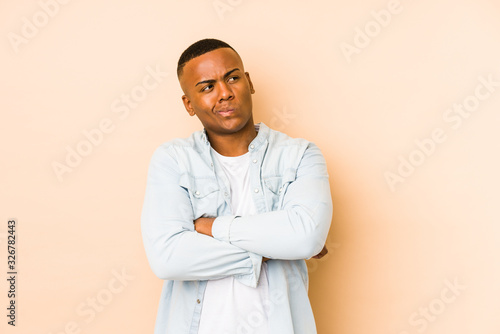 Young latin man isolated on beige background frowning face in displeasure, keeps arms folded.
