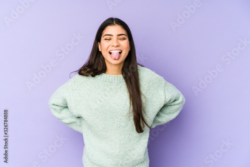 Young indian woman isolated on purple background funny and friendly sticking out tongue.
