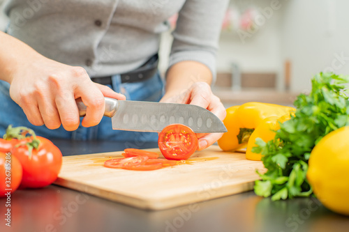 Woman is cutting tomatoes on cut board on kitchen.