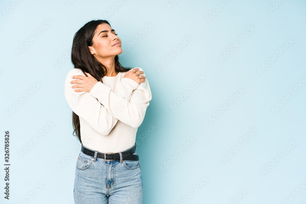 Young indian woman isolated on blue background hugs, smiling carefree and happy. Young indian woman isolated on blue background hugs, smiling carefree and happy.