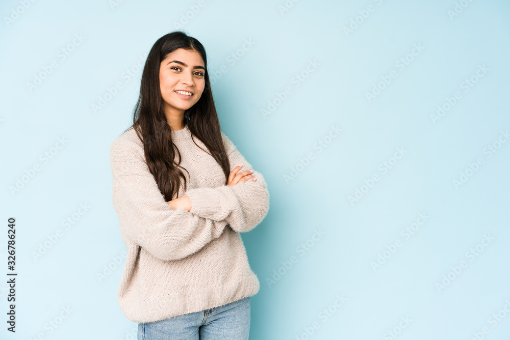 Young indian woman isolated on blue background who feels confident, crossing arms with determination.