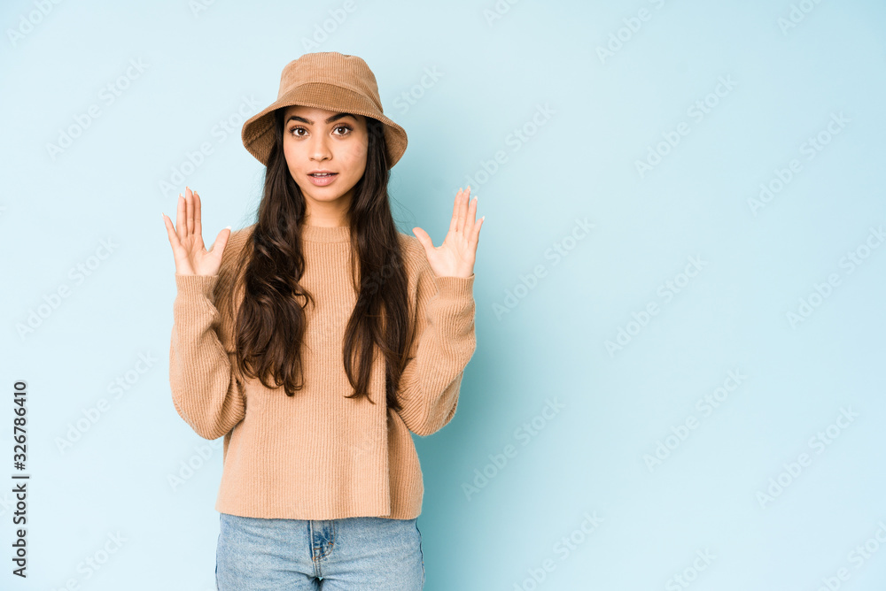 Young indian woman wearing a hat isolated on blue background holding something little with forefingers, smiling and confident. Young indian woman wearing a hat isolated on blue background holding something little with forefingers, smiling and confident.