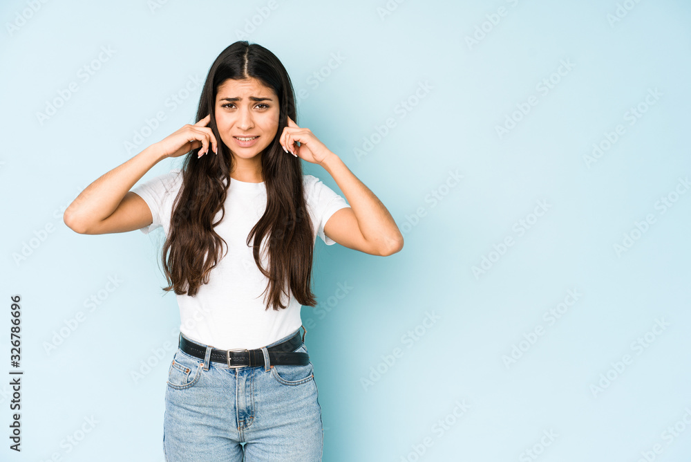 Young indian woman on blue background covering ears with fingers, stressed and desperate by a loudly ambient. Young indian woman on blue background covering ears with fingers, stressed and desperate by a loudly ambient.