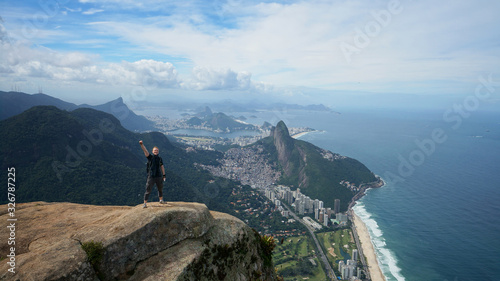 Happy traveler on the top of Pedra da Gavea mountain with panoramic aerial view to the Rio de Janeiro landscape in Brazil.