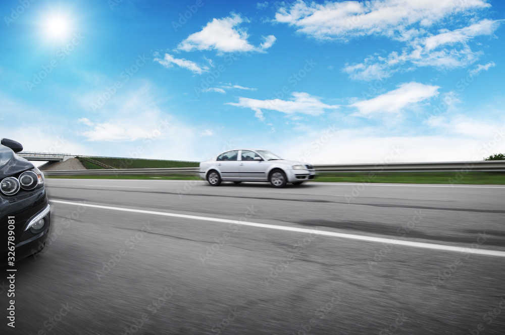 Fototapeta premium Cars driving fast on the countryside road against a blue sky with the sun