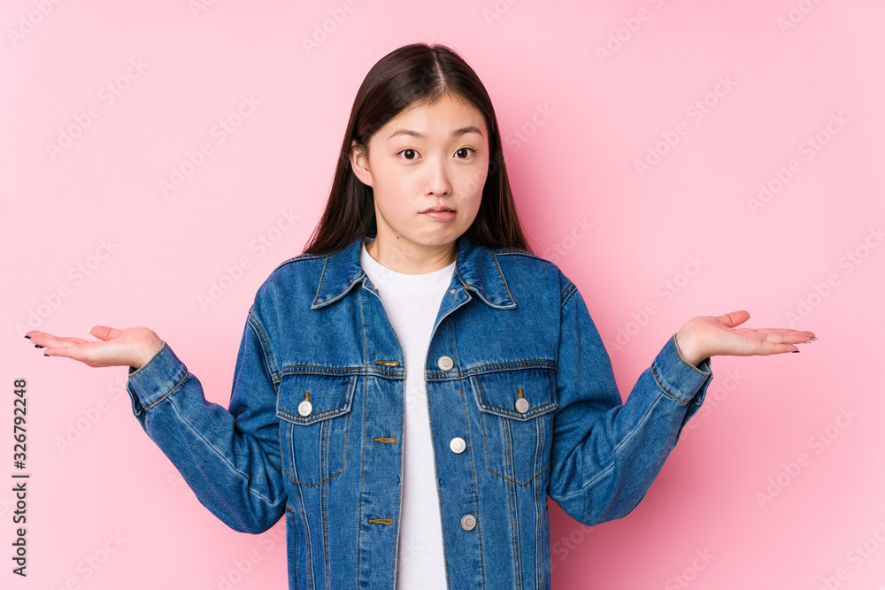 Young chinese woman posing in a pink background isolated confused and doubtful shrugging shoulders to hold a copy space. Young chinese woman posing in a pink background isolated confused and doubtful shrugging shoulders to hold a copy space.