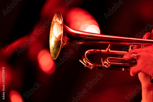 A trumpet player playing the trumpet in a big band concert on stage with red stage lights with bokeh in the background