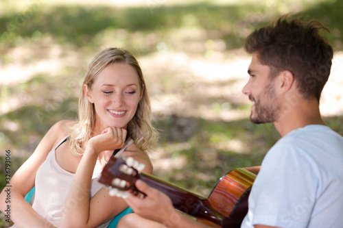 man playing guitar for young lady sat in park