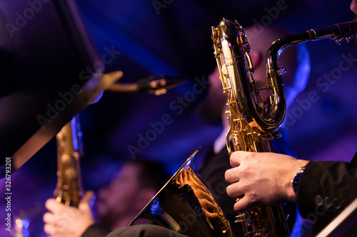 A baritone saxophone player playing their horn during a jazz concert in a venue with blue and purple stage lights photo