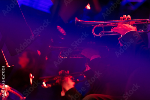 Musicians of a big band trumpet section are laying down some smooth jazz all dressed in concert black during a live show in a venue with red lights and blue lights making streaks in fron of the camera photo