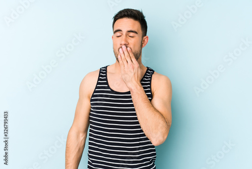 Young caucasian man isolated on blue background yawning showing a tired gesture covering mouth with hand.