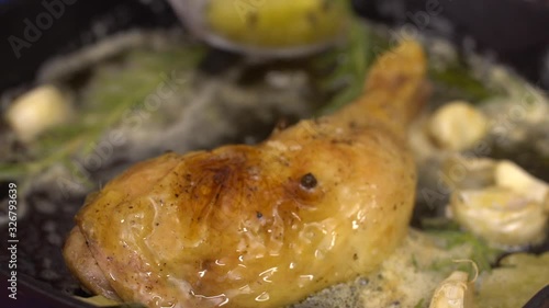 Chef pouring chicken leg with melted butter mixture with thyme, bay leaf and pepper, close up view