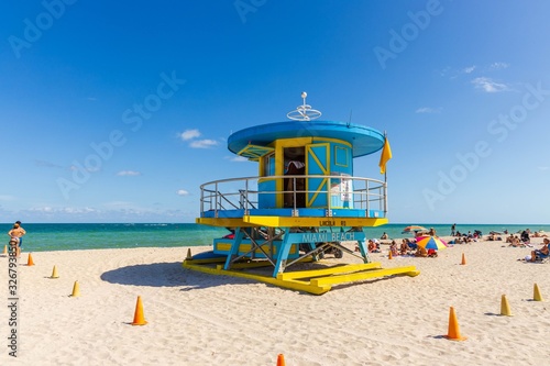 People on Miami beach on beautiful sunny day. Sand beach, tourists and yellow lifeguard tower on blue Atlantic ocean merging with blue sky background. Miami. USA. © Alex