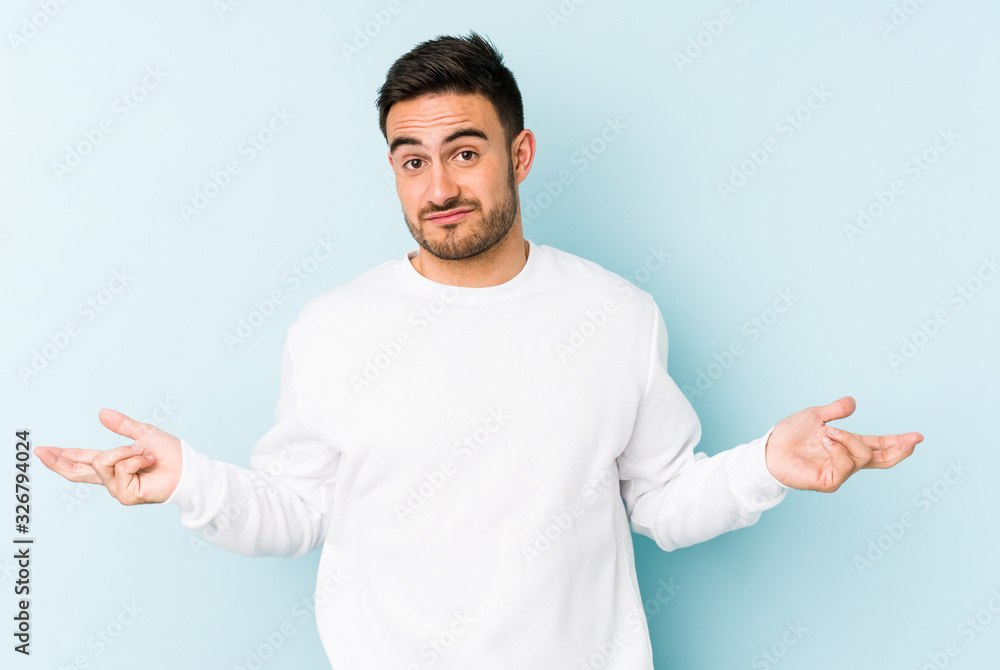 Young caucasian man isolated on blue background doubting and shrugging shoulders in questioning gesture. Young caucasian man isolated on blue background doubting and shrugging shoulders in questioning gesture.