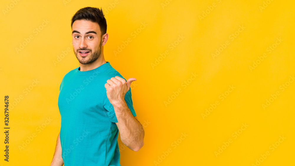 Young caucasian man isolated on yellow bakground points with thumb finger away, laughing and carefree. Young caucasian man isolated on yellow bakground points with thumb finger away, laughing and carefree.