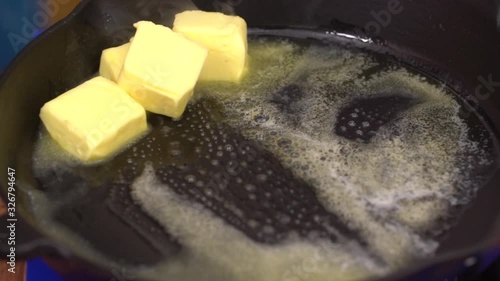 Closeup shot of iron pan on gas stove with big chunks of butter melting on grill surface.