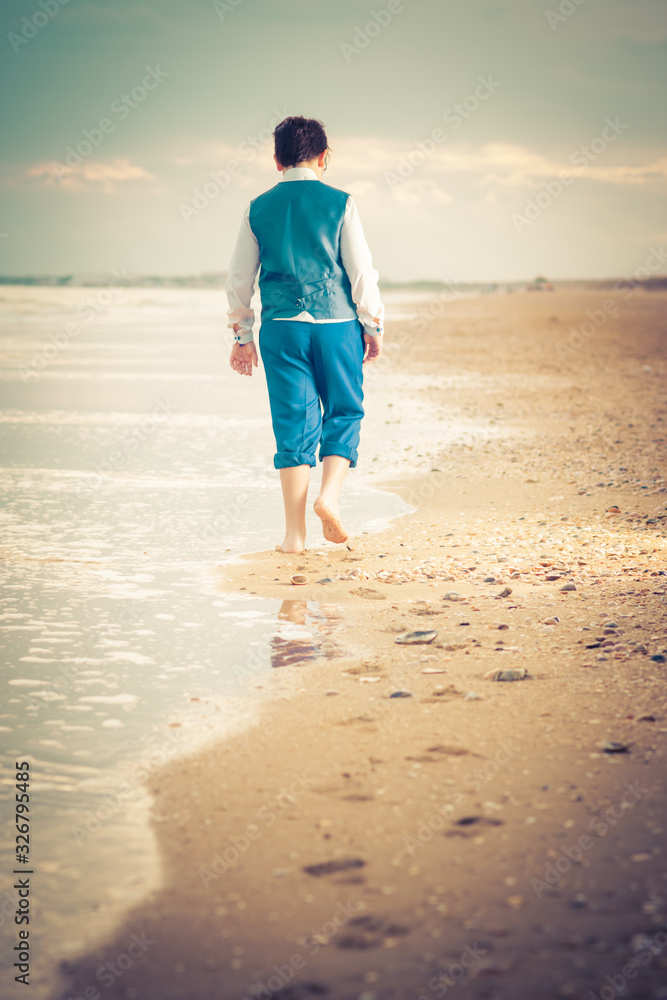 The young Caucasian walks barefoot on the beach near the sea, footprints in the sand