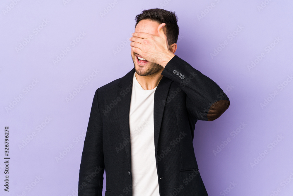 Young caucasian man isolated on purple background covers eyes with hands, smiles broadly waiting for a surprise. Young caucasian man isolated on purple background covers eyes with hands, smiles broadly waiting for a surprise.