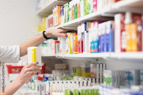 Pharmacist holding medicine box and capsule pack in pharmacy drugstore.