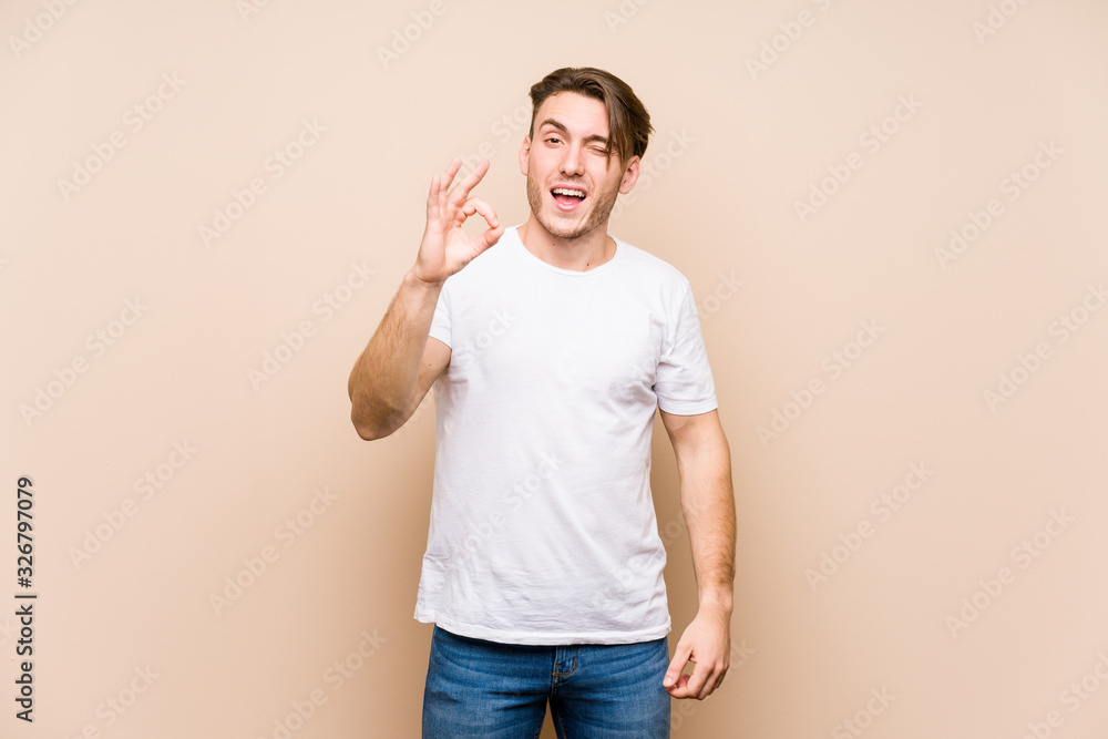 Young caucasian man posing isolated winks an eye and holds an okay gesture with hand. Young caucasian man posing isolated winks an eye and holds an okay gesture with hand.