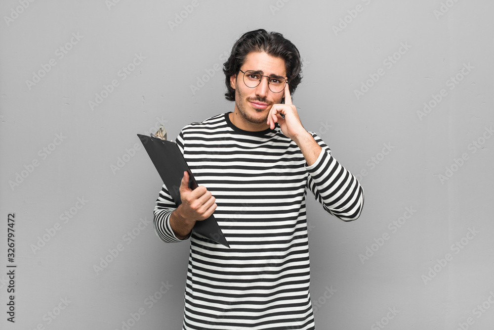 Young employee man holding an inventory focused on a task, keeping forefingers pointing head. Young employee man holding an inventory focused on a task, keeping forefingers pointing head.