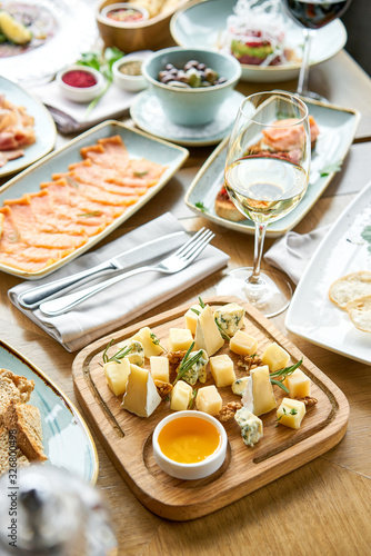 Cheese plate. Focus on delicious cheese mix with walnuts, honey on wooden table. Various snacks and antipasti on the table. Restaurant menu.