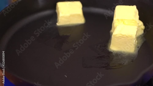 Closeup shot of iron pan on gas stove with big chunks of butter melting on grill surface.