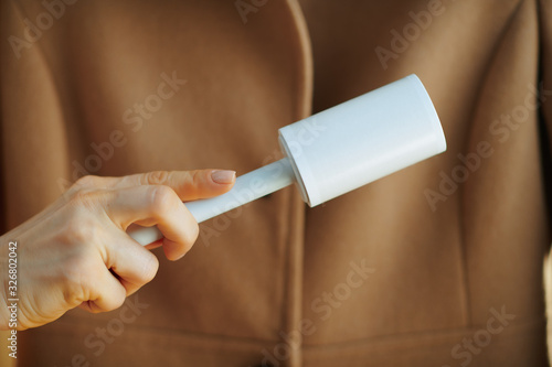 Closeup on smiling woman cleaning coat with lint roller