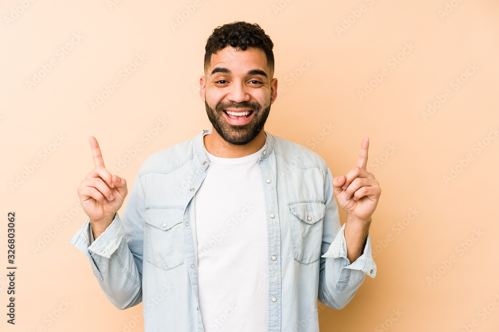 Young mixed race arabic man isolated indicates with both fore fingers up showing a blank space. Young mixed race arabic man isolated indicates with both fore fingers up showing a blank space.
