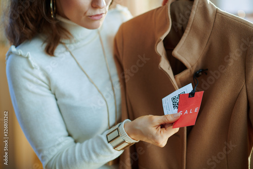 Closeup on woman examines sale price tag on beige coat
