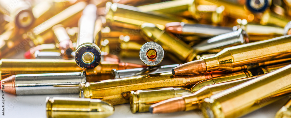 Naklejka premium Pile of fire bullets or ammunition banner or panorama on dark stone table. Hand guns weapon in background. Many projectiles into 9mm gun.