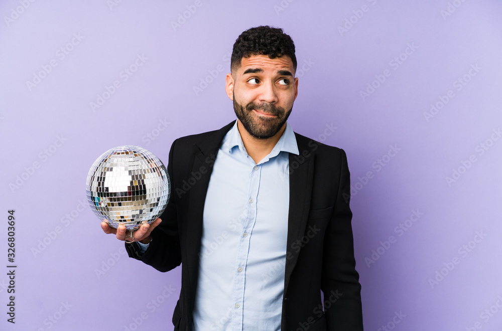 Young latin man holding a party ball isolated Young latin man holding a waffle isolated confused, feels doubtful and unsure.< mixto > Young latin man holding a party ball isolated Young latin man holding a waffle isolated confused, feels doubtful and unsure.< mixto >