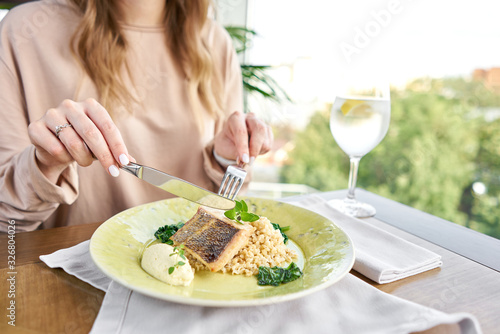 Roasted Pike perch with spelt and Polish sauce. Lunch in a restaurant, a woman eats delicious and healthy food. Dish decorated with a spinach. Restaurant menu