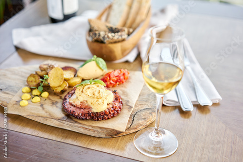 Roasted octopus BBQ and Baked potato with a glass of Grapa. Wooden plate. Restaurant menu