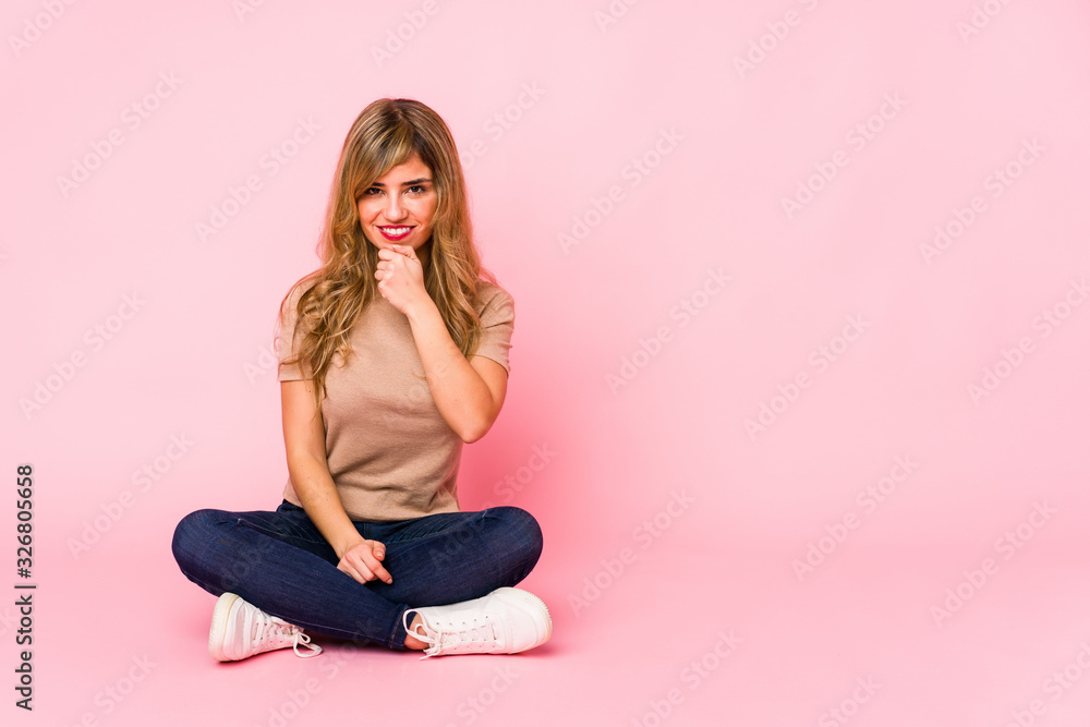 Young blonde caucasian woman sitting on a pink studio smiling happy and confident, touching chin with hand.