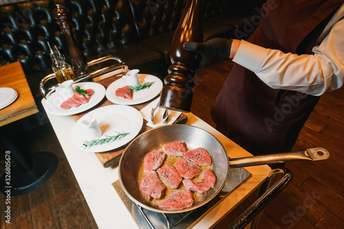 Chef seasoning with peppermill and frying tenderloin on a pan photo