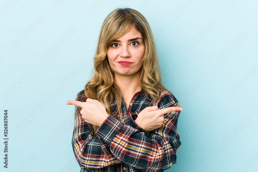 Young blonde caucasian woman points sideways, is trying to choose between two options. Young blonde caucasian woman points sideways, is trying to choose between two options.