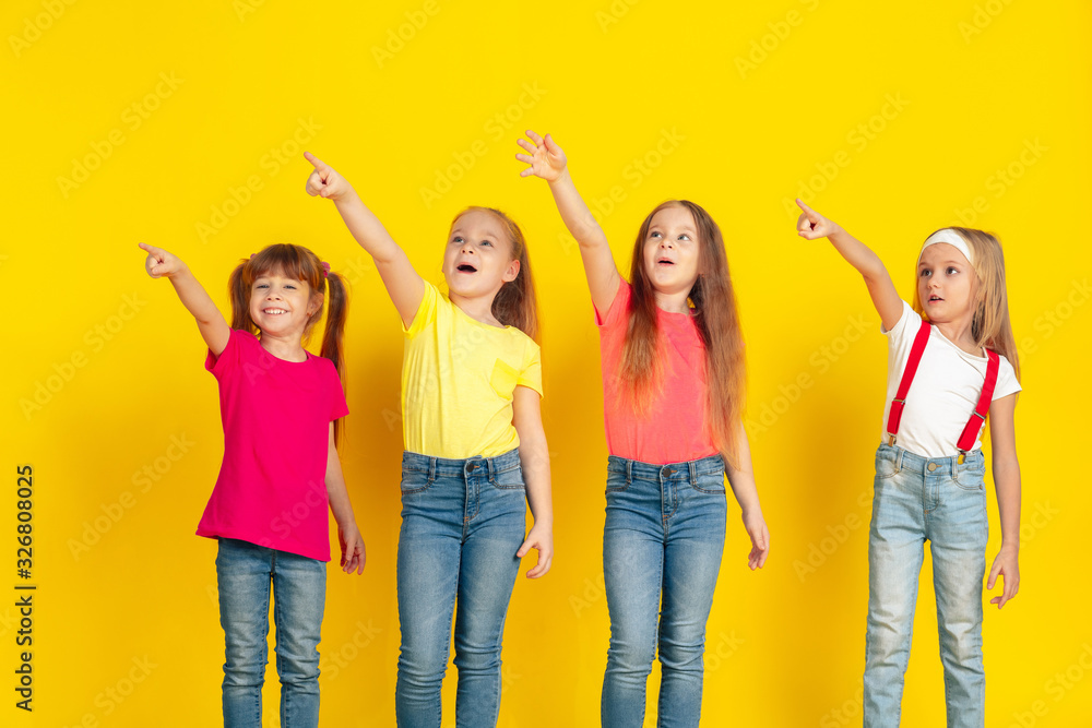 Obraz premium Pointing. Happy children playing and having fun together on yellow studio background. Caucasian kids in bright clothes looks playful, laughting, smiling. Concept of education, childhood, emotions.