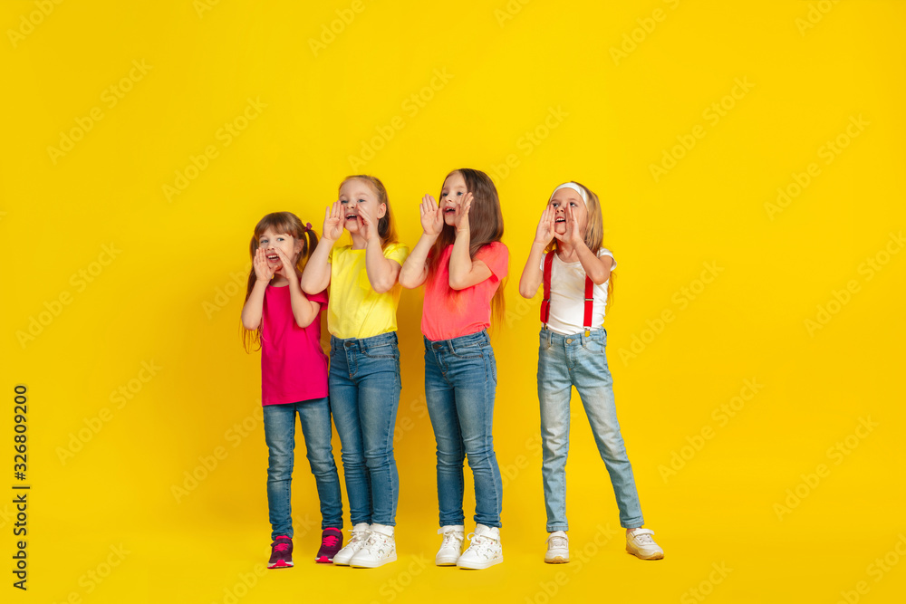 Calling. Happy children playing and having fun together on yellow studio background. Caucasian kids in bright clothes looks playful, laughting, smiling. Concept of education, childhood, emotions. Calling. Happy children playing and having fun together on yellow studio background. Caucasian kids in bright clothes looks playful, laughting, smiling. Concept of education, childhood, emotions.