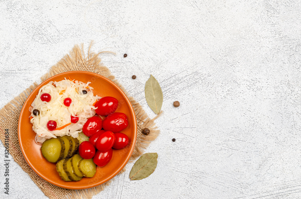 Homemade tasty fermented products on a plate - sauerkraut, tomatoes, pickles, peppercorns, bay leaf on a white background, copy space Homemade tasty fermented products on a plate - sauerkraut, tomatoes, pickles, peppercorns, bay leaf on a white background, copy space