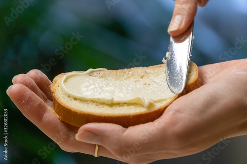 woman's hand holds a slice of white bread and spreads butter with a knife close-up