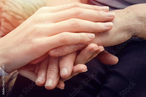 Hands of a young girl holding the hands of an old, elderly woman close up. Concept two generations of age women