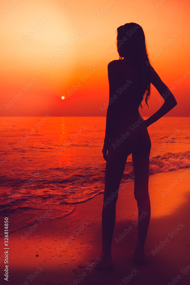 Black slhouette of slim girl on the sea beach. People meets the dawn. Summer vacation.