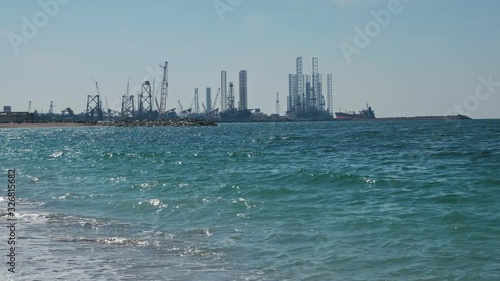 Construction of oil production towers in the Persian Gulf. Desert edifilled beach, waves. The concept of ocean pollution, global warming, carbon production.