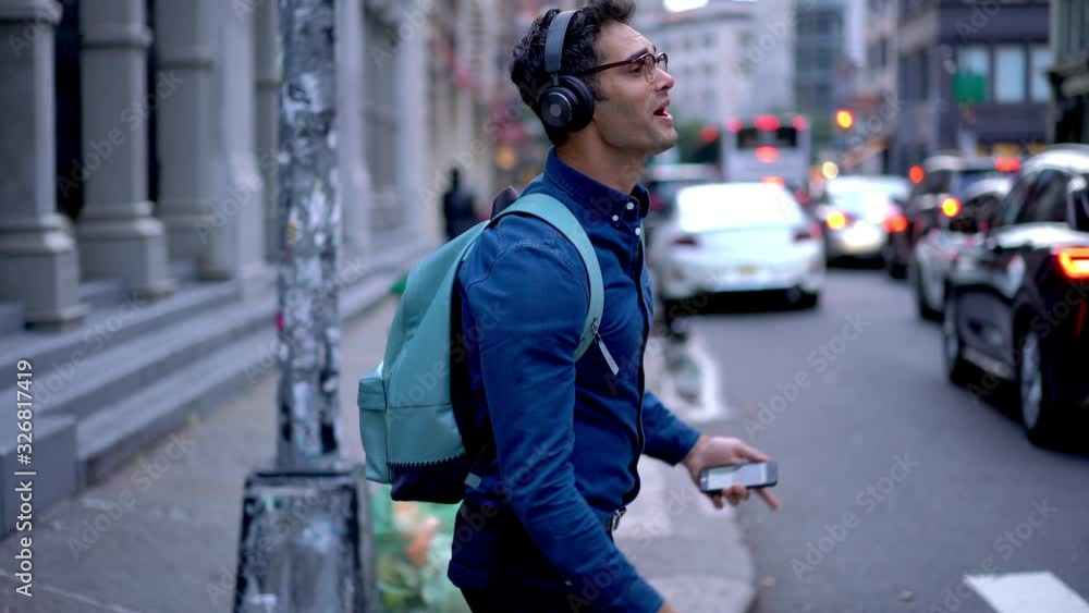 Joyful Spanish hipster guy in trendy glasses feeling happiness during leisure day in city downtown, smiling male music lover dancing and signing at urbanity connected to 4g on smartphone for using app Joyful Spanish hipster guy in trendy glasses feeling happiness during leisure day in city downtown, smiling male music lover dancing and signing at urbanity connected to 4g on smartphone for using app