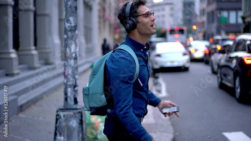 Joyful Spanish hipster guy in trendy glasses feeling happiness during leisure day in city downtown, smiling male music lover dancing and signing at urbanity connected to 4g on smartphone for using app