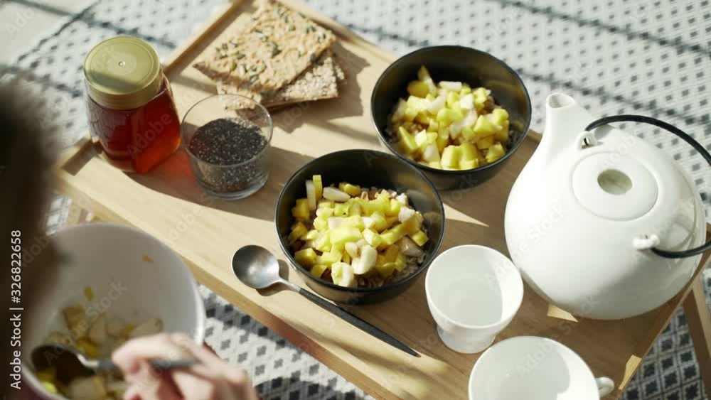 Breakfast on the terrace. Picnic on the sunny terrace. Healthy breakfast. Girl adds fruits to oatmeal. Tasty healthy porridge with nuts, fruits and honey. Morning tea. Eco products. Diet breakfast. Breakfast on the terrace. Picnic on the sunny terrace. Healthy breakfast. Girl adds fruits to oatmeal. Tasty healthy porridge with nuts, fruits and honey. Morning tea. Eco products. Diet breakfast.