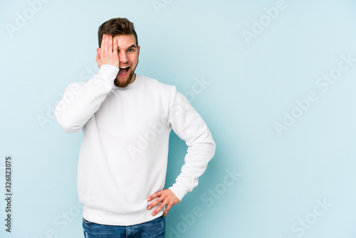 Young caucasian man isolated on blue background having fun covering half of face with palm.