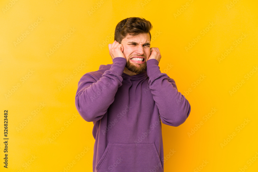 Young caucasian man isolated on yellow background covering ears with hands. Young caucasian man isolated on yellow background covering ears with hands.